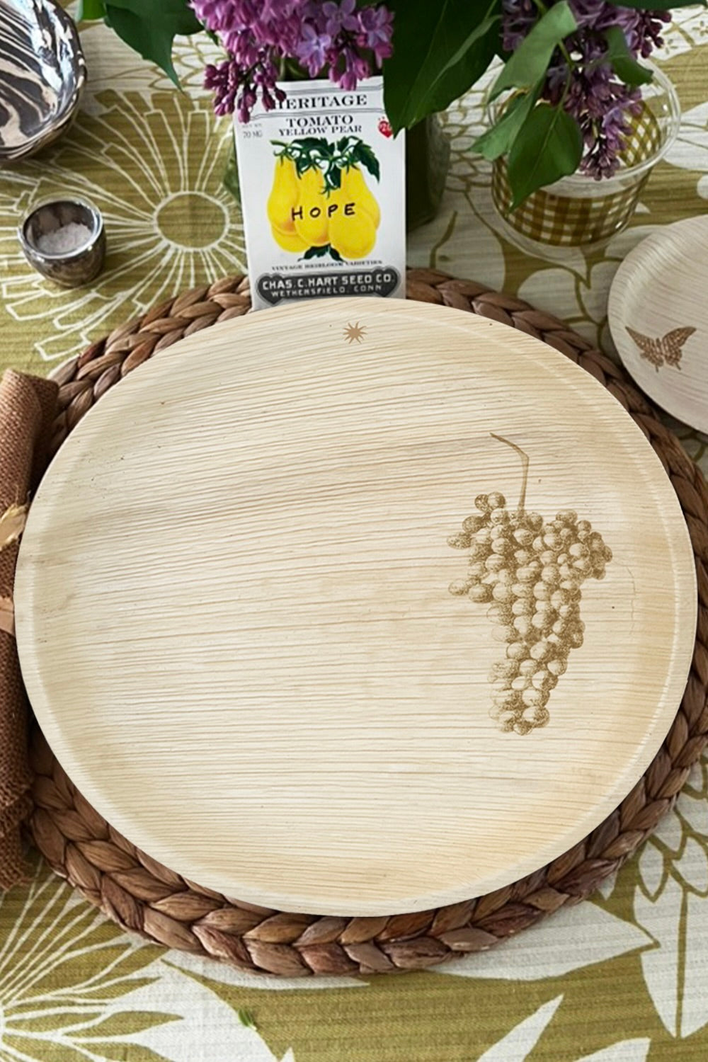 maaterra compostable palm leaf plate with grapes design on a woven charger