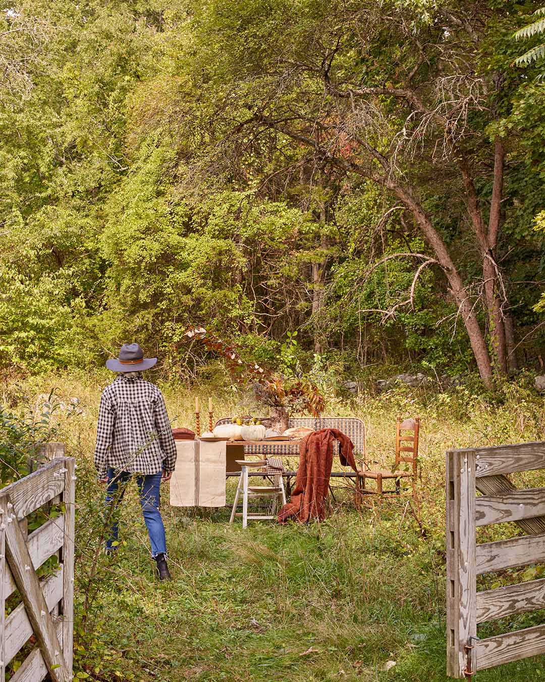 Scenic backyard with trees and natural grass with a women walking towards a set table. 