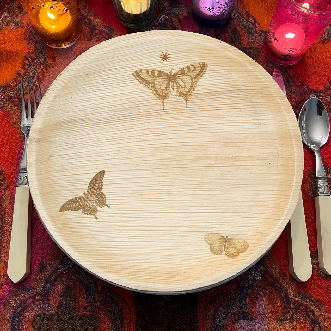 maaterra compostable palm leaf plate with butterfly wreath design on a red tablecloth with candles