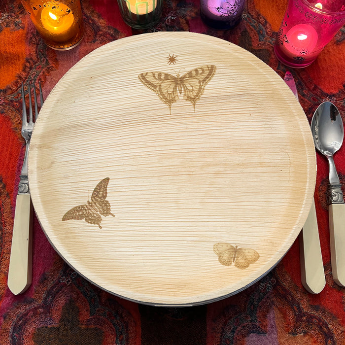 maaterra compostable palm leaf plate with butterfly wreath design on a red tablecloth with candles