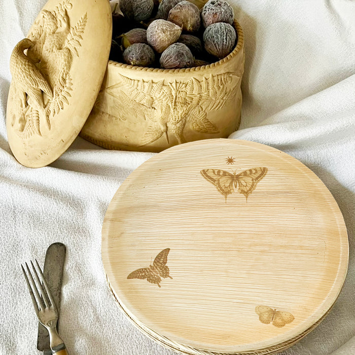 maaterra compostable palm leaf plate with butterfly wreath design on a white tablecloth