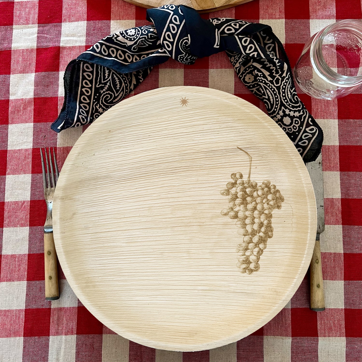 maaterra compostable palm leaf plate with grapes design on a gingham tablecloth
