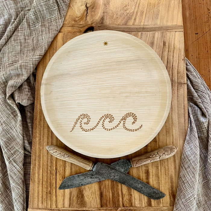 maaterra compostable palm leaf plate with waves design on a bread board