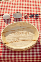 Wooden plate with 'COOKOUT' engraving on a red and white checkered tablecloth.