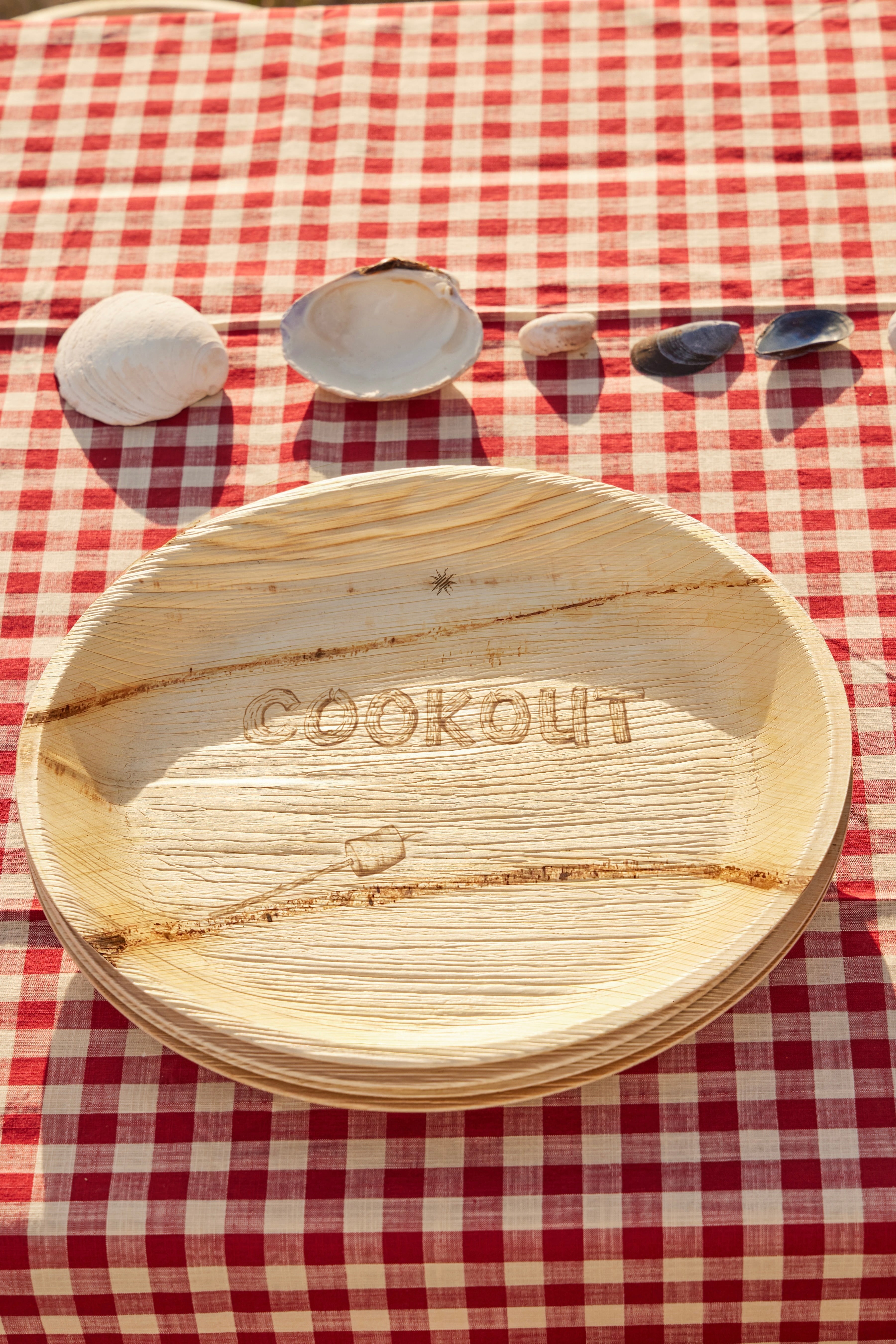 Wooden plate with 'COOKOUT' engraving on a red and white checkered tablecloth.