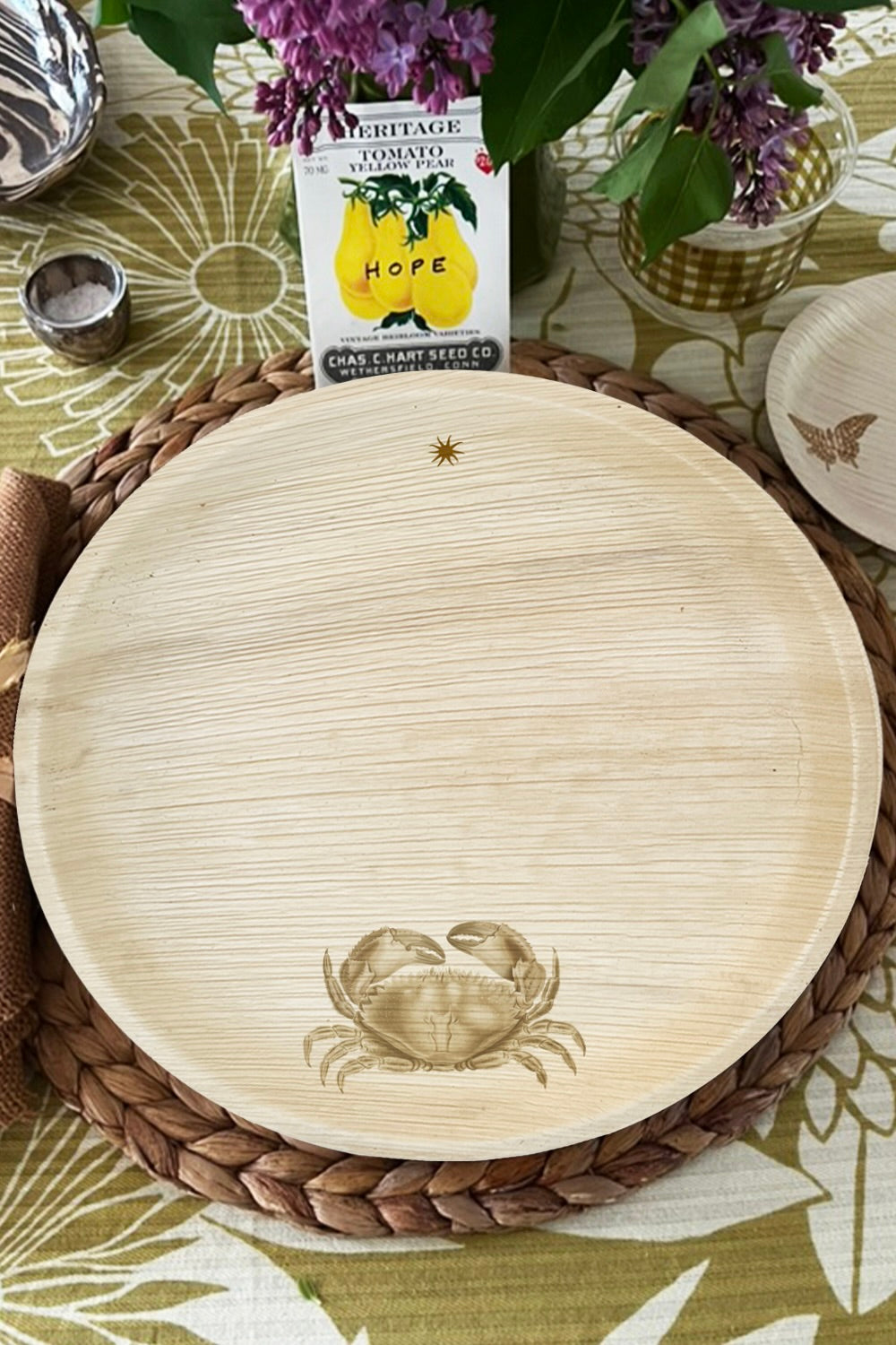 Round wooden tray with crab design on a woven placemat with flowers and seed packet in the background.