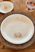 Wooden plate with crab design on a woven tray, compostable cup and sustainable plate in the background