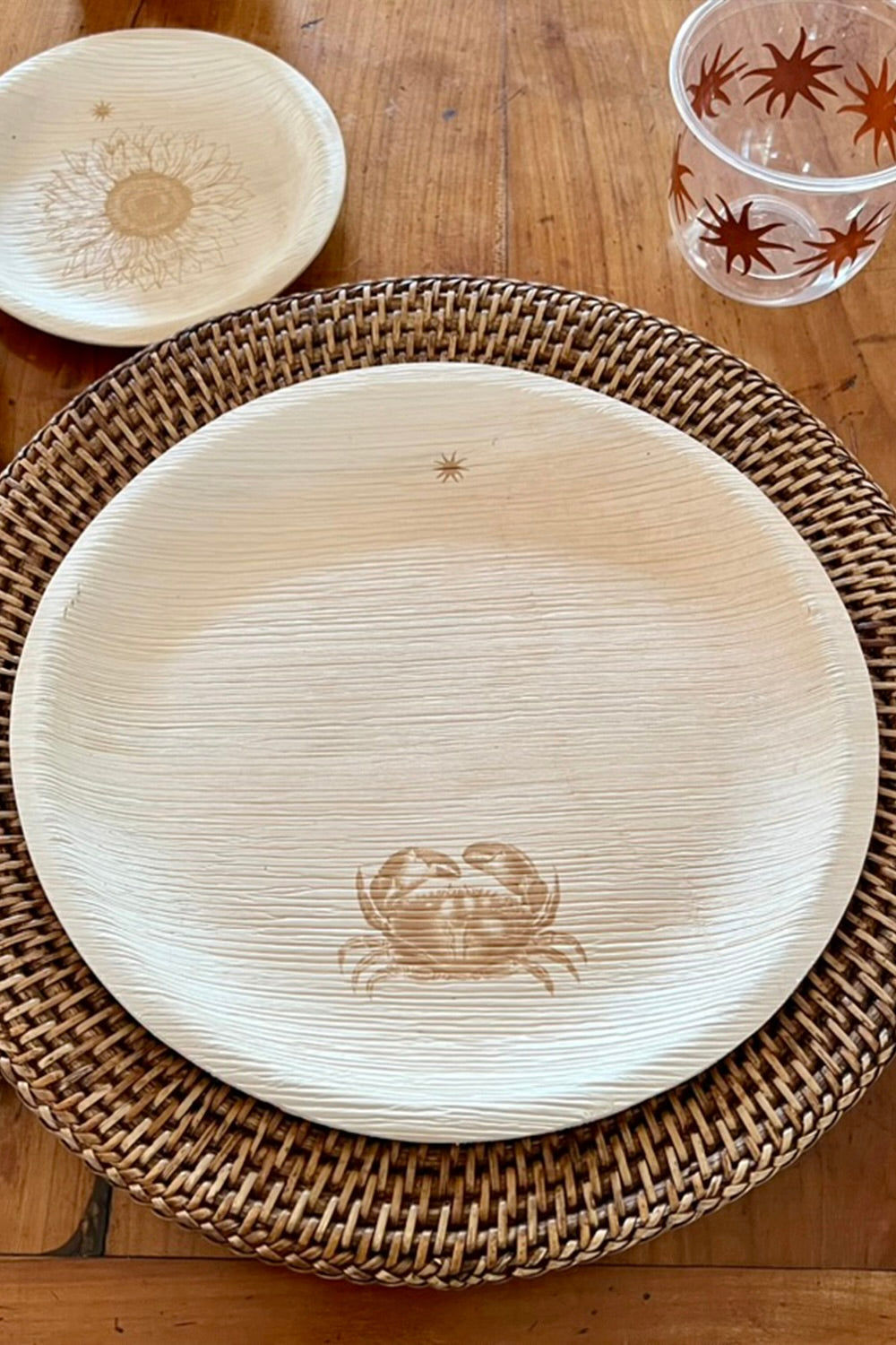 Wooden plate with crab design on a woven tray, compostable cup and sustainable plate in the background