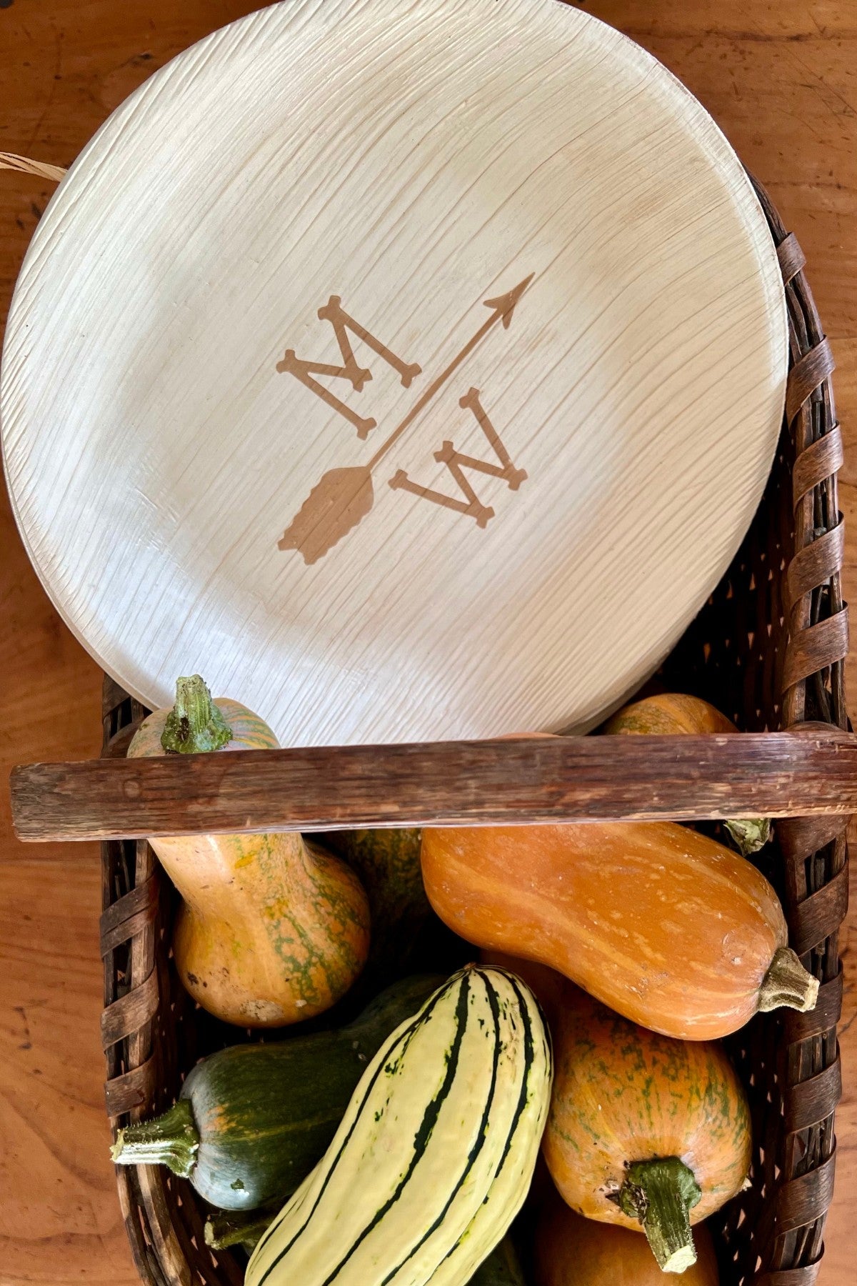 maaterra palm leaf plate with custom single arrow design on a basket filled with pumpkins. 
