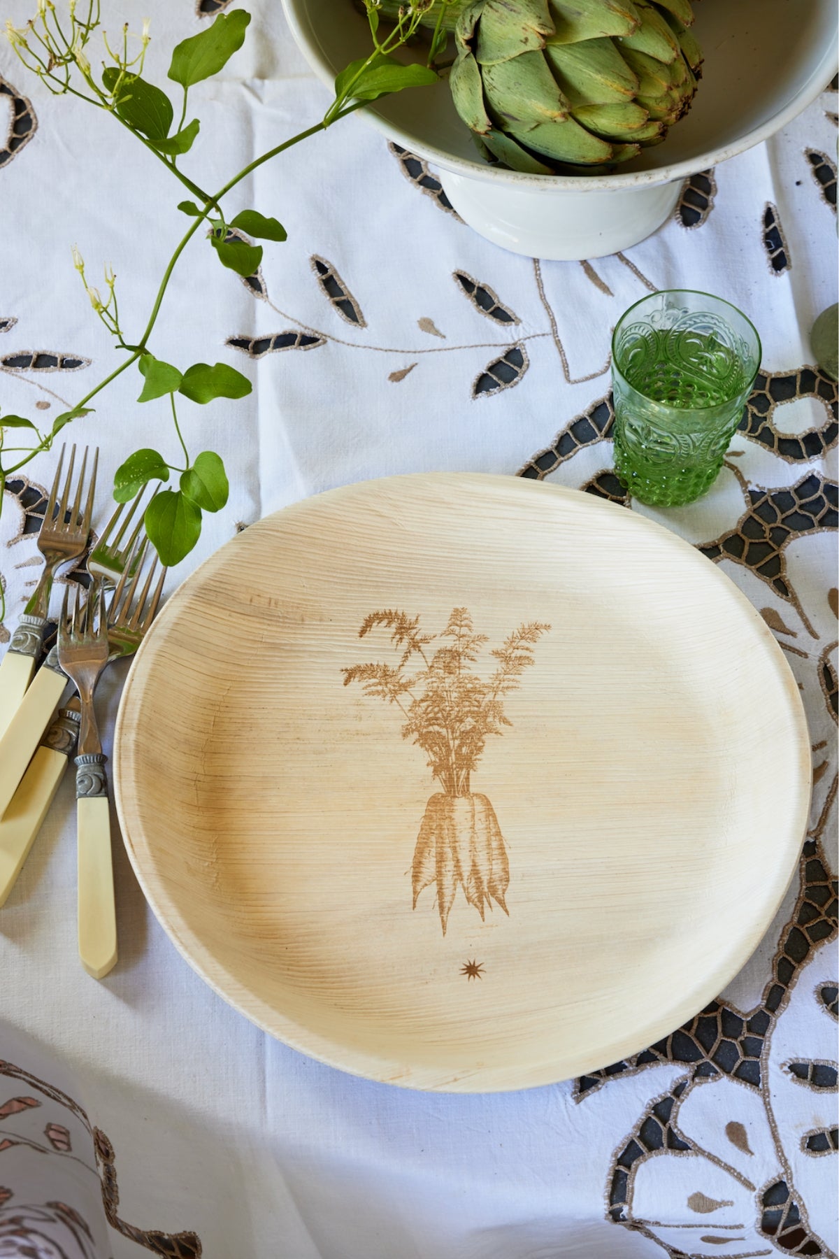 Palm leaf plate with engraved carrot design on a patterned tablecloth with many green plants. 