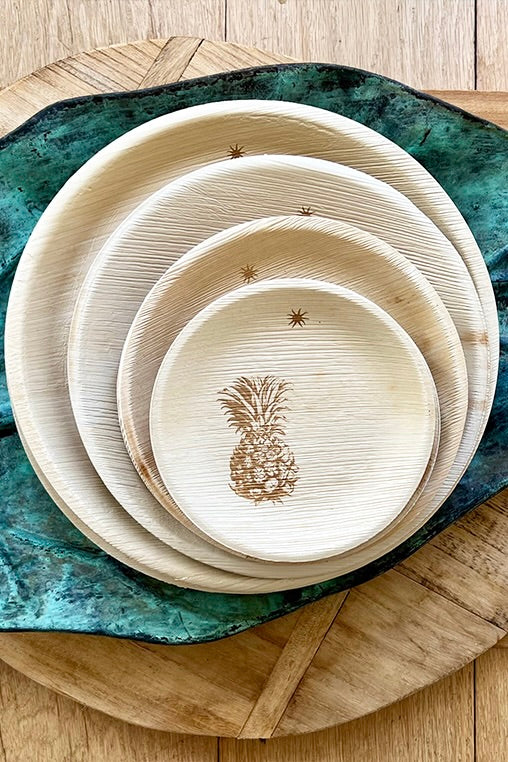 Set of round, natural-colored plates with a pineapple design on a green textured surface.