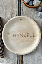 maaterra compostable palm leaf plate with 'THANKFUL' engraving on a textured surface with fruits and striped fabric.