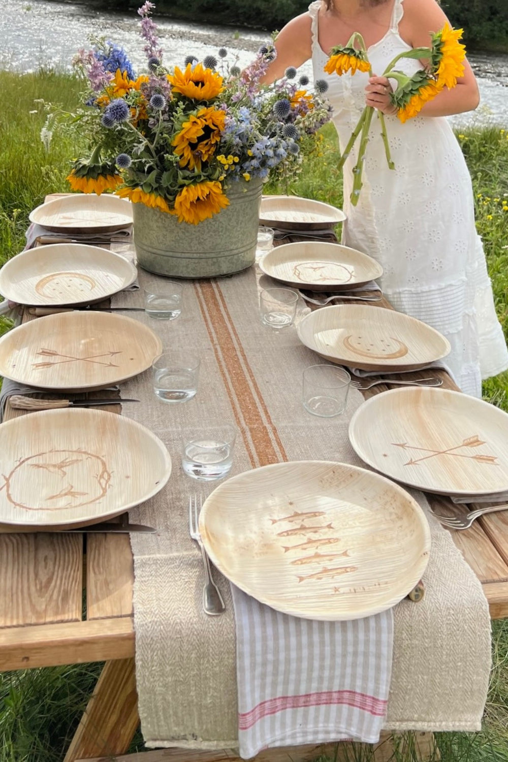 maaterra palm leaf plates on a table with a floral arrangement placed in a grass field. 